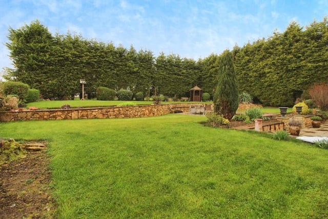 The attractive gardens feature well-maintained lawns, surrounded by trees.