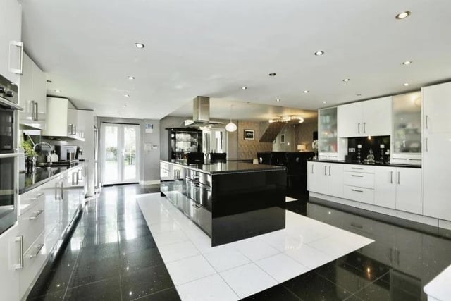 Here is another sparkling, high-gloss, open-plan kitchen. Black granite work surfaces complement a range of modern, white wall and base units. There is an integrated double oven and microwave, five-ring induction hob, dishwasher, washing machine, wine fridge, inset spotlights and granite floor tiles. A central island has cupboards beneath.