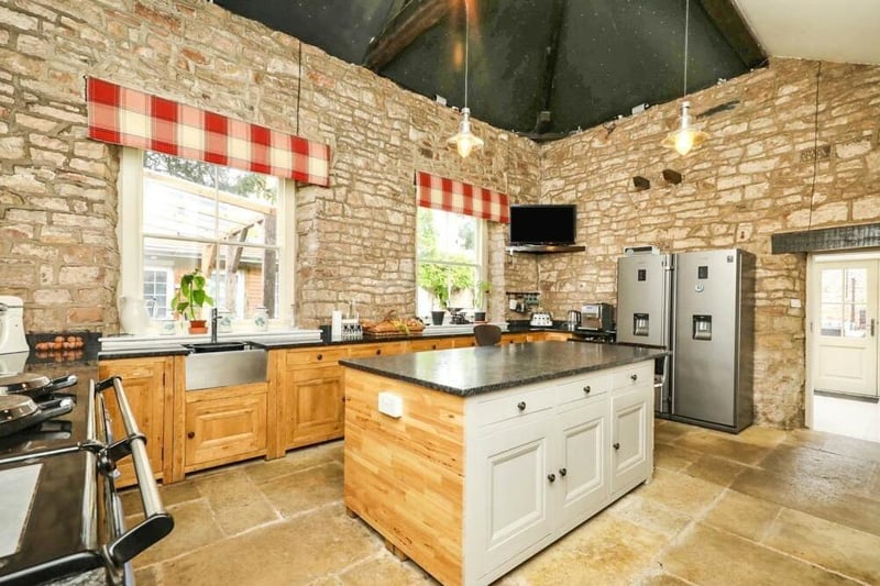 The kitchen is also distinguished by a vaulted ceiling with exposed, original beams. The room is fitted with a range of wall and base units, along with work surfaces incorporating an inset sink unit, while a central island offers a focal point..