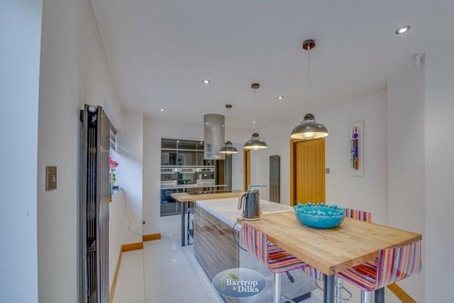 The breakfast kitchen features a central island with a fitted electric hob and extractor. There is also an integrated dishwasher, quartz work surfaces, a breakfast bar with seating and a sink unit with a mixer tap.