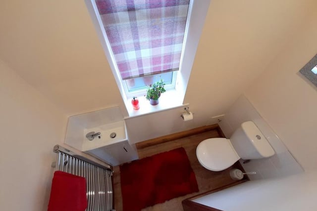 An overhead shot of the downstairs cloakroom. It comprises a low-flush WC, wash hand basin with cupboard underneath, chrome heated towel-rail, laminate floor, coving and recessed spotlights to the ceiling.