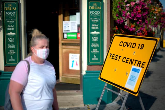Pedestrians wearing facemasks walks past a sign for a Covid-19 test centre  (Photo by DANIEL LEAL-OLIVAS / AFP)