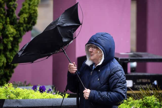 A pedestrian struggles with her umbrella against the wind (Photo by ANDY BUCHANAN/AFP via Getty Images)