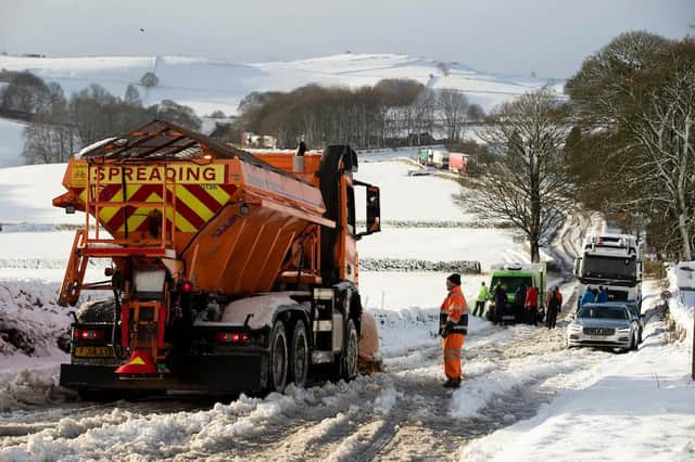 A gritter lorry stops to wait as people help to push an Asda delivery van stuck on the A515 after eavy snow fall in the Derbyshire Peak District.