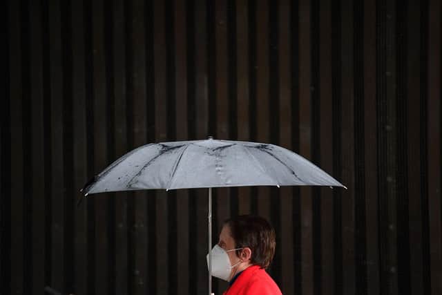 A pedestrian wearing a face mask shelters under an umbrella (Photo by JUSTIN TALLIS/AFP via Getty Images)