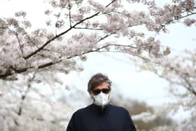 A man wearing a face mask walks amongst blossom trees (Photo by Hollie Adams/Getty Images)