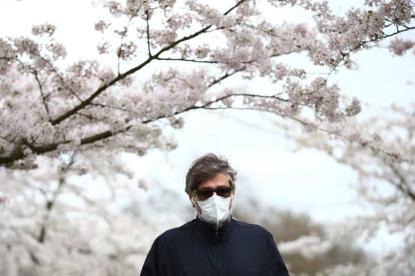 A man wearing a face mask walks amongst blossom trees (Photo by Hollie Adams/Getty Images)