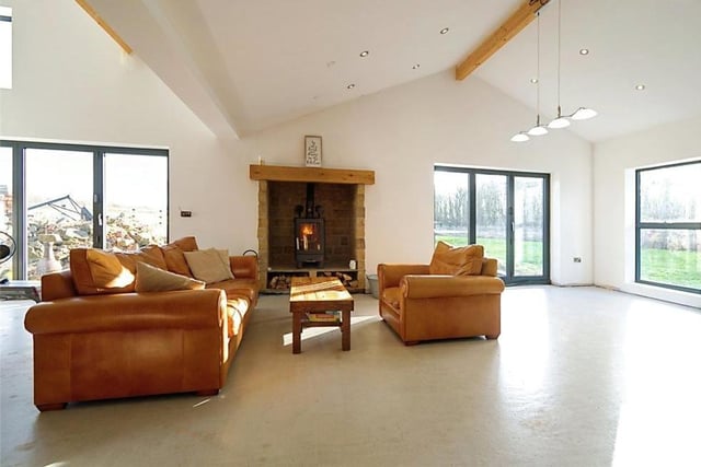 Our tour of the barn conversion begins in the open-plan kitchen/sitting room/dining room. This is the spacious sitting room area, with its feature fireplace and large windows and doors overlooking the grounds outside.