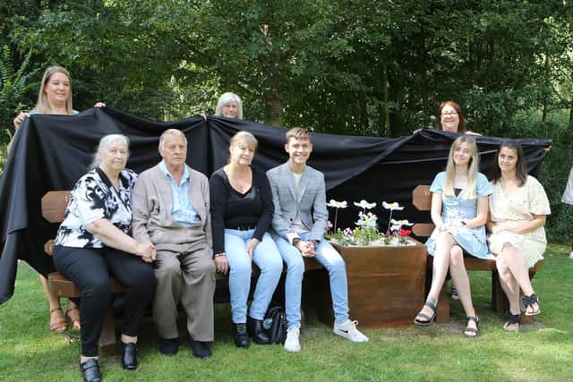 Nicola and family of her late husband Ian on the new seat. Community Unity Project's Zara Skidmore, April Johnson and Elaine Streets are are holding the sheet at the back.